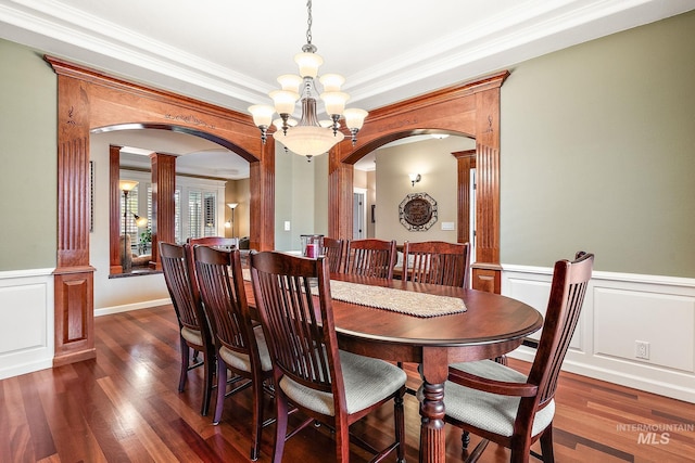 dining room with arched walkways, dark wood-style flooring, a chandelier, and a wainscoted wall