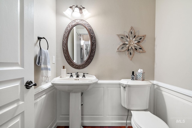 half bath featuring a wainscoted wall, a decorative wall, and toilet