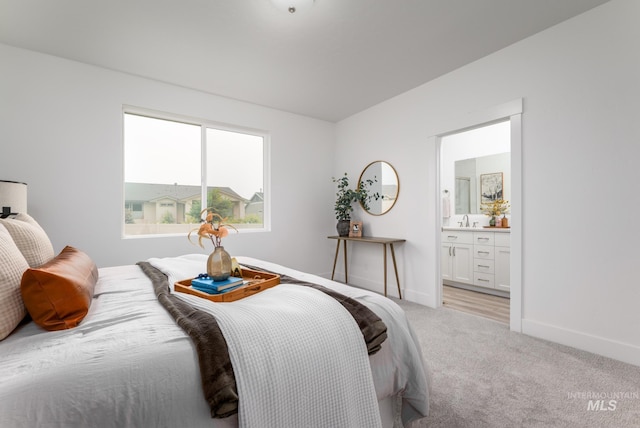 bedroom featuring light carpet, ensuite bath, baseboards, and a sink