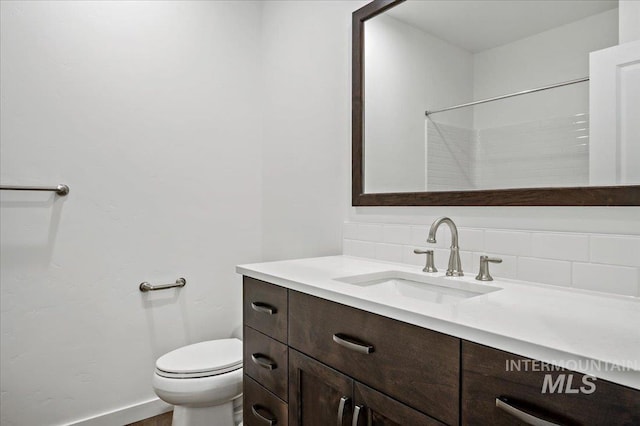 bathroom featuring baseboards, backsplash, toilet, and vanity