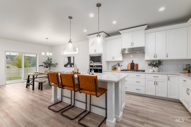 kitchen featuring under cabinet range hood, a sink, light countertops, built in microwave, and stainless steel gas stovetop