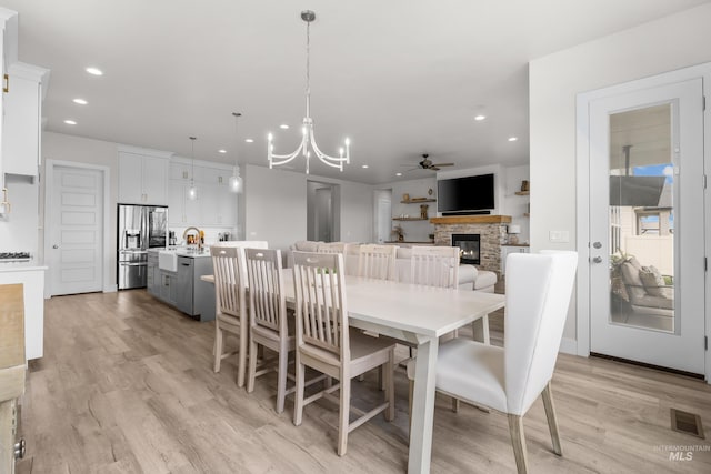 dining room featuring ceiling fan with notable chandelier, light hardwood / wood-style flooring, and a stone fireplace