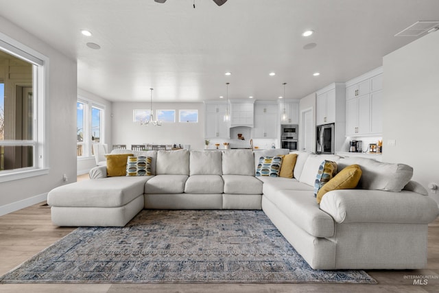 living room with ceiling fan with notable chandelier, sink, and light hardwood / wood-style flooring