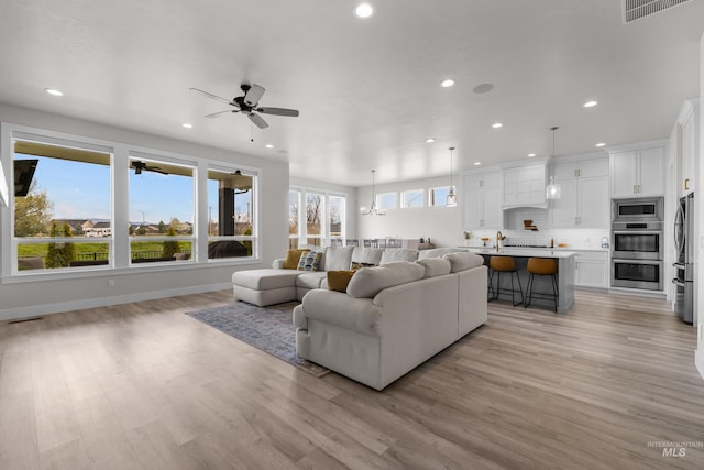 living room with ceiling fan with notable chandelier and light wood-type flooring