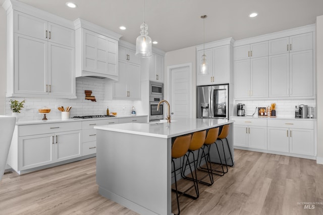 kitchen featuring light hardwood / wood-style flooring, an island with sink, a breakfast bar area, white cabinets, and appliances with stainless steel finishes