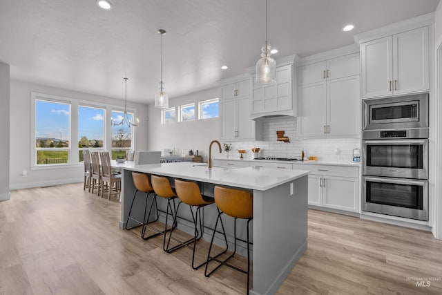 kitchen featuring decorative light fixtures, a center island with sink, and white cabinets