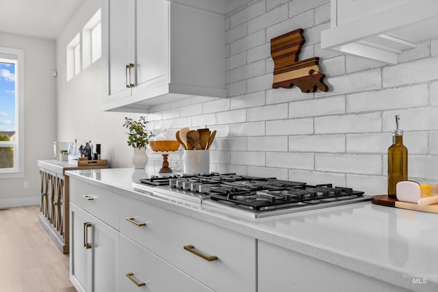 kitchen featuring white cabinets, stainless steel gas cooktop, light wood-type flooring, decorative backsplash, and light stone countertops