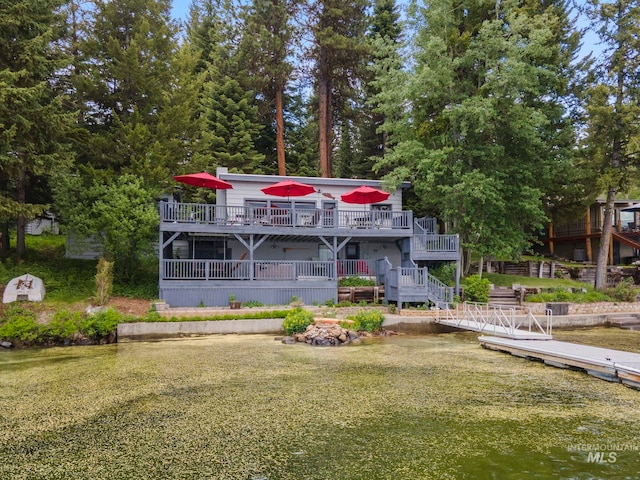 rear view of property featuring a deck with water view and a lawn