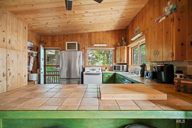 kitchen featuring sink, wooden walls, appliances with stainless steel finishes, tile counters, and wood ceiling