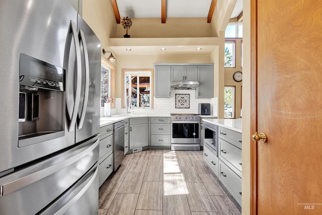 kitchen featuring stainless steel appliances, gray cabinets, decorative backsplash, light countertops, and beamed ceiling