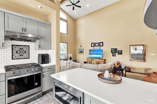 kitchen with appliances with stainless steel finishes, under cabinet range hood, gray cabinets, high vaulted ceiling, and ceiling fan