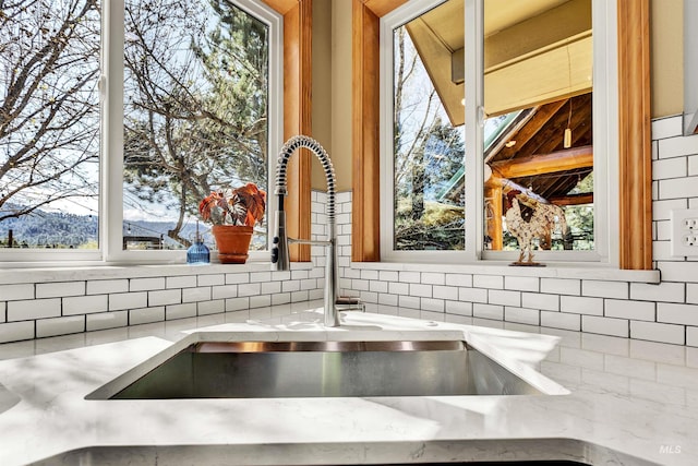 kitchen view of decorative backsplash, a sink, and light stone countertops