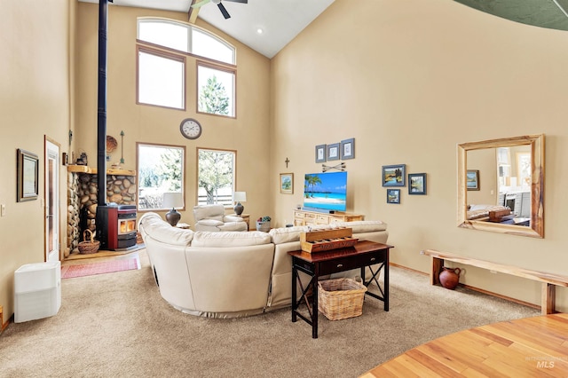 living room featuring a wood stove, high vaulted ceiling, plenty of natural light, wood finished floors, and ceiling fan