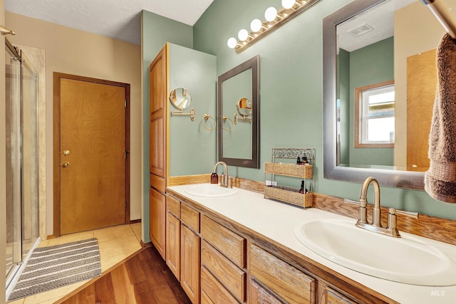 full bathroom with double vanity, a shower stall, and wood finished floors