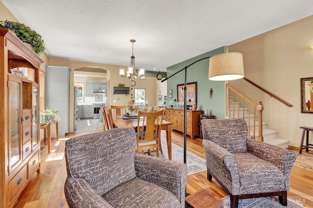 dining room featuring a chandelier, arched walkways, light wood finished floors, and stairway