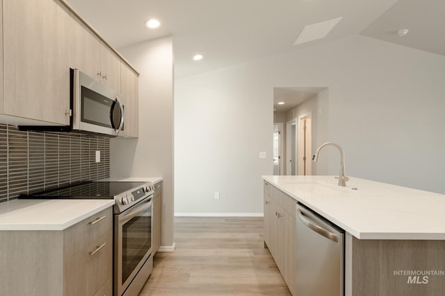 kitchen featuring an island with sink, light hardwood / wood-style flooring, appliances with stainless steel finishes, and vaulted ceiling