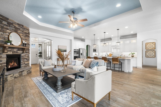 5853 W Venetian Dr, Eagle, ID 83616 - living area featuring a raised ceiling, a ceiling fan, arched walkways, a stone fireplace, and light wood-style floors
