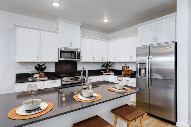 kitchen featuring sink, white cabinets, a kitchen breakfast bar, stainless steel appliances, and light wood-type flooring