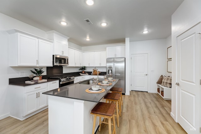 kitchen featuring sink, white cabinets, a kitchen breakfast bar, stainless steel appliances, and a center island with sink