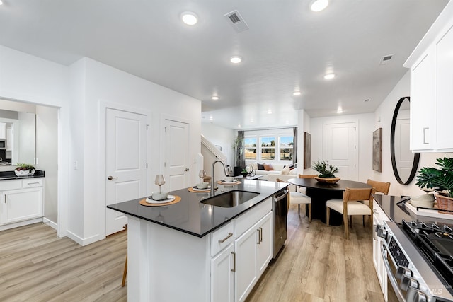 kitchen featuring appliances with stainless steel finishes, sink, white cabinets, light hardwood / wood-style floors, and a center island with sink