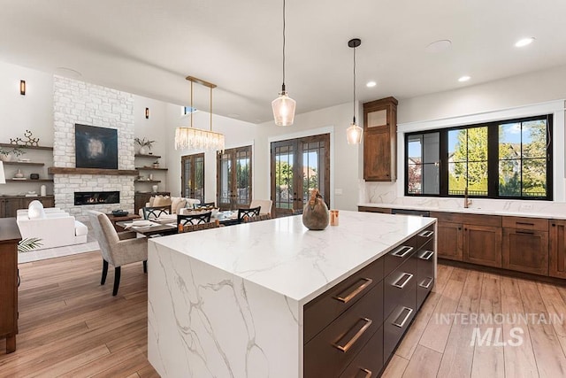 1195 N Arrano Farms Ln, Eagle, ID 83616 - kitchen with light wood-type flooring, a fireplace, a kitchen island, hanging light fixtures, and recessed lighting