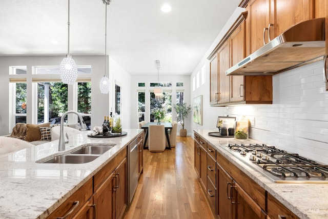 kitchen featuring brown cabinets, a sink, under cabinet range hood, stainless steel appliances, and light wood-style flooring