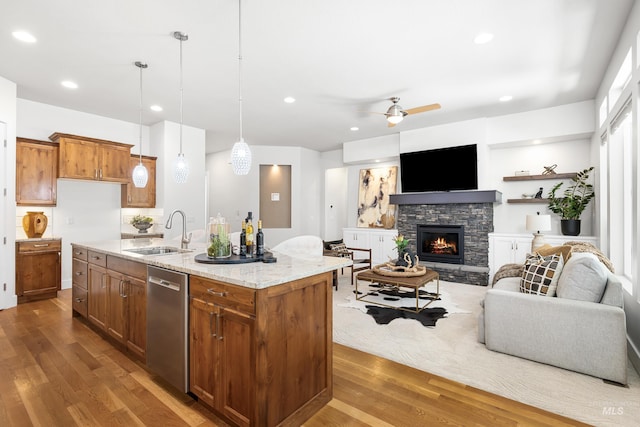 kitchen featuring stainless steel dishwasher, brown cabinetry, wood finished floors, open floor plan, and a sink