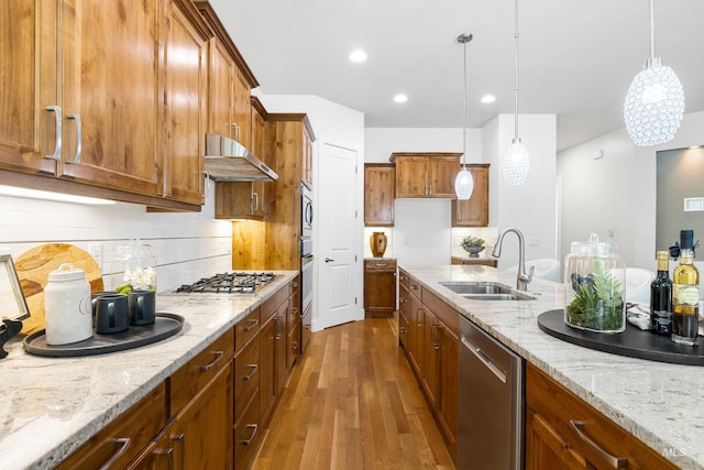 kitchen featuring brown cabinetry, decorative light fixtures, a sink, under cabinet range hood, and stainless steel appliances