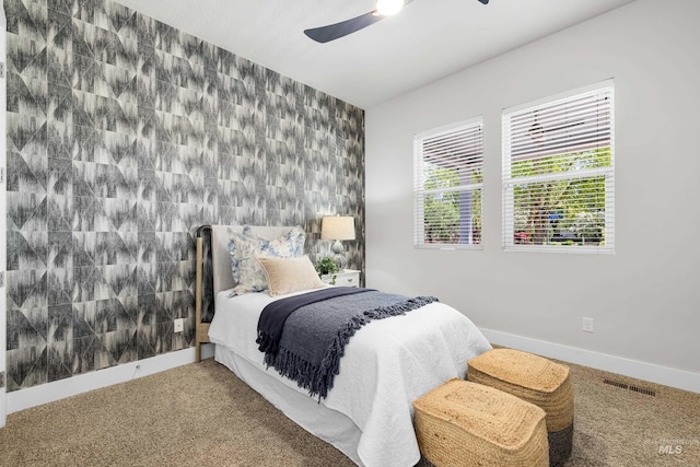 carpeted bedroom with baseboards, an accent wall, a ceiling fan, and visible vents