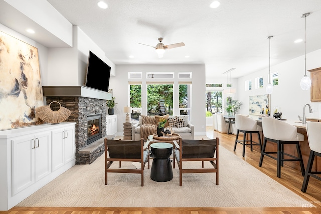 living room with ceiling fan, light wood-style flooring, recessed lighting, and a stone fireplace