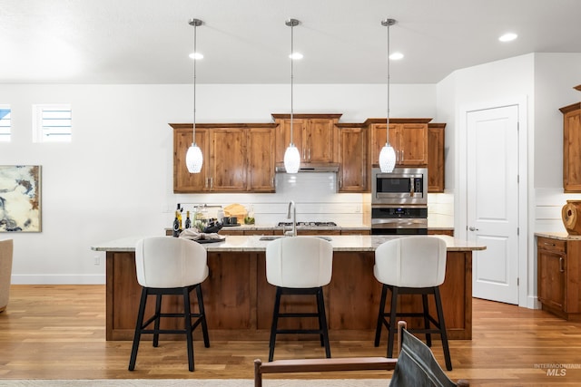 kitchen with light wood-style floors, under cabinet range hood, a sink, appliances with stainless steel finishes, and backsplash