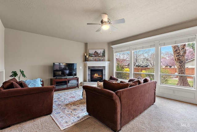 living room featuring a ceiling fan, a tile fireplace, light carpet, and a textured ceiling