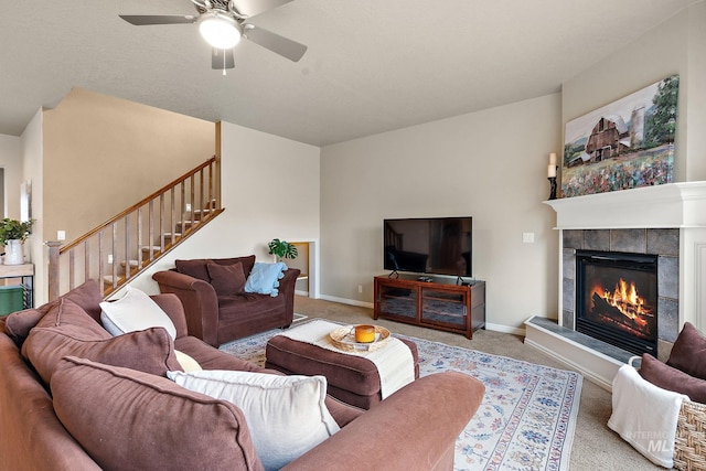 carpeted living room featuring a tile fireplace, ceiling fan, baseboards, and stairs