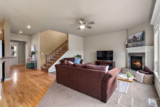 living area featuring baseboards, a tiled fireplace, ceiling fan, light wood finished floors, and stairs