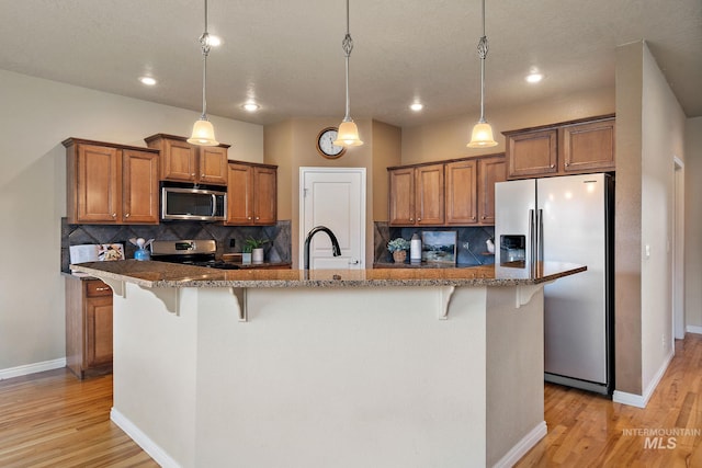 kitchen with light wood-type flooring, brown cabinets, a breakfast bar area, and appliances with stainless steel finishes