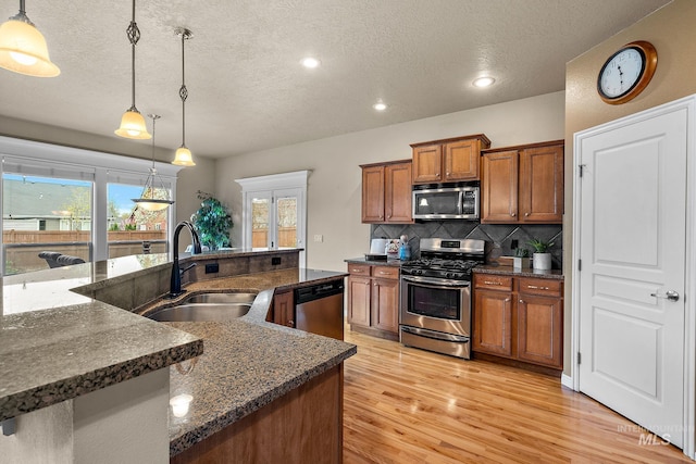 kitchen featuring light wood-style floors, brown cabinetry, a sink, stainless steel appliances, and decorative backsplash
