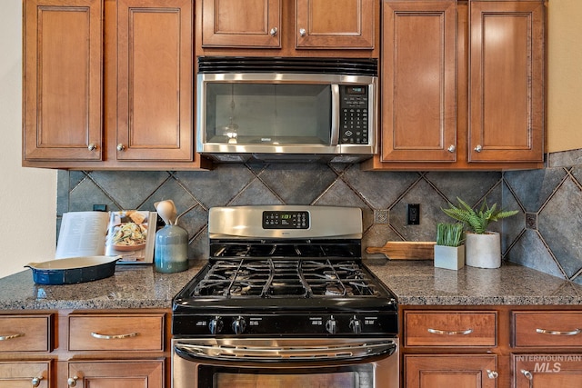 kitchen featuring dark stone countertops, brown cabinets, decorative backsplash, and stainless steel appliances