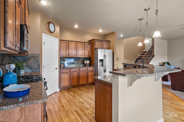 kitchen featuring a kitchen breakfast bar, light wood-style floors, brown cabinetry, appliances with stainless steel finishes, and pendant lighting