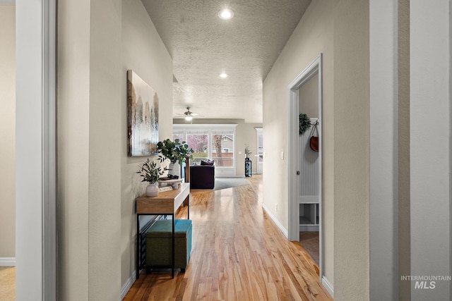 hall featuring baseboards, recessed lighting, wood finished floors, and a textured ceiling