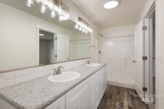 bathroom featuring dual sinks, oversized vanity, a shower, tasteful backsplash, and hardwood / wood-style flooring