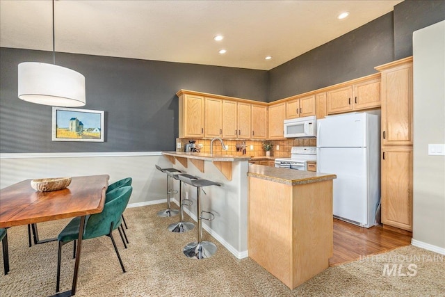 kitchen featuring hanging light fixtures, kitchen peninsula, light brown cabinetry, white appliances, and tasteful backsplash