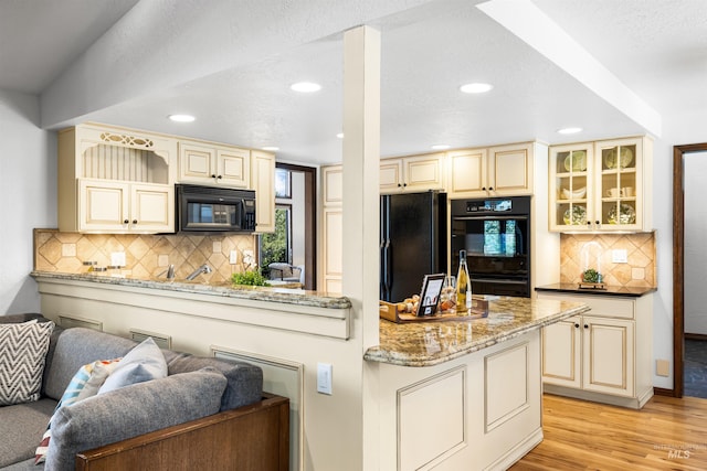 kitchen featuring cream cabinetry, black appliances, recessed lighting, light wood-type flooring, and glass insert cabinets