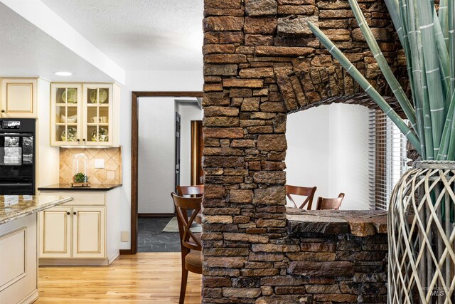 kitchen featuring cream cabinets, light wood finished floors, glass insert cabinets, tasteful backsplash, and baseboards