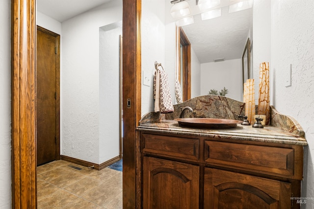 bathroom with a textured wall, vanity, tile patterned floors, and baseboards