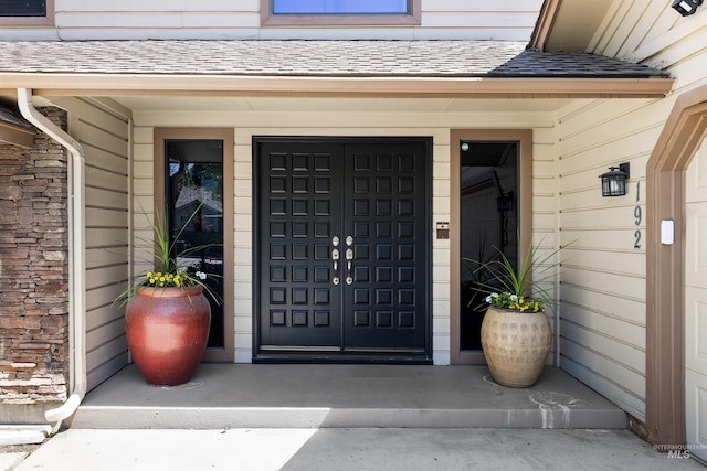 view of exterior entry with roof with shingles