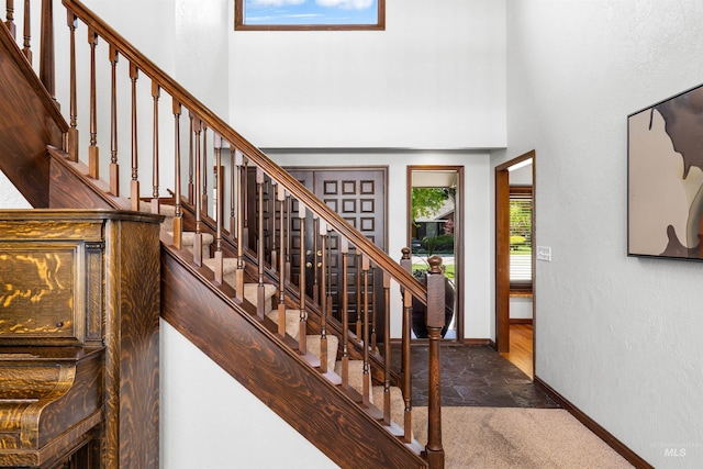 stairway with baseboards, a high ceiling, stone tile flooring, and carpet