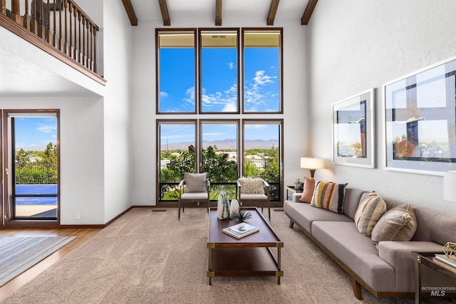 carpeted living area with a towering ceiling, beamed ceiling, plenty of natural light, baseboards, and wood finished floors