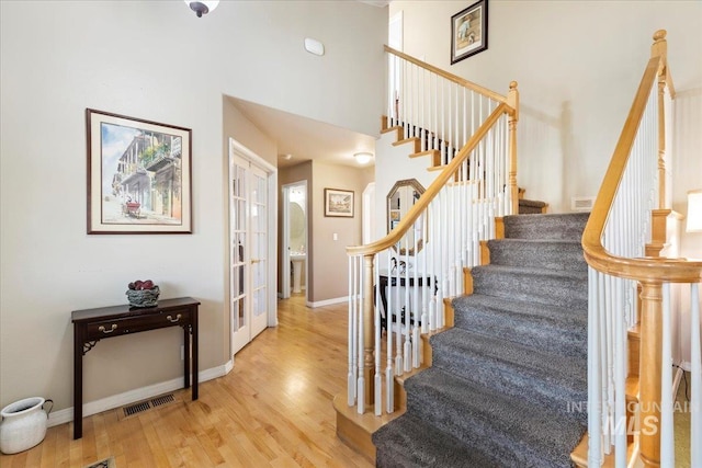 stairs featuring french doors, wood-type flooring, and a high ceiling