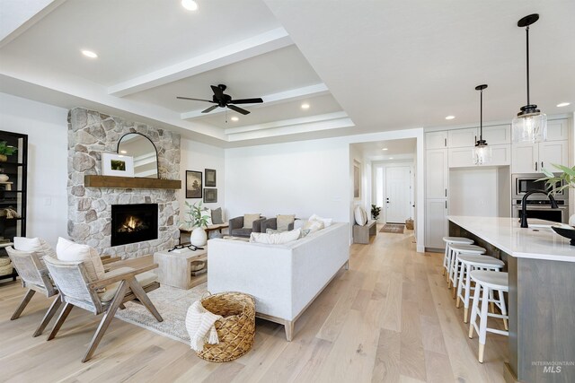 living area with beamed ceiling, a ceiling fan, recessed lighting, a fireplace, and light wood finished floors