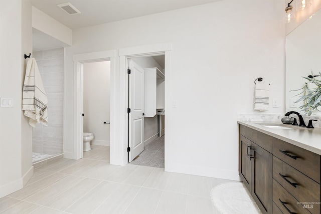 full bathroom with visible vents, toilet, a tile shower, baseboards, and vanity